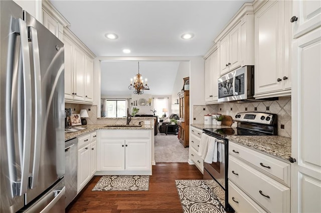 kitchen with an inviting chandelier, a sink, a peninsula, stainless steel appliances, and dark wood-type flooring