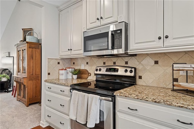kitchen featuring light stone countertops, light colored carpet, white cabinets, stainless steel appliances, and decorative backsplash