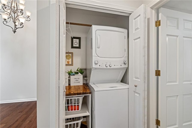 clothes washing area featuring laundry area, stacked washing maching and dryer, a notable chandelier, dark wood-style floors, and baseboards