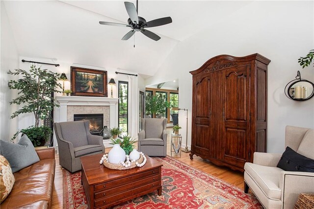 living area featuring a ceiling fan, vaulted ceiling, a glass covered fireplace, and light wood finished floors