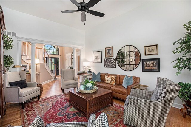 living area featuring stairs, wood finished floors, baseboards, ornate columns, and a ceiling fan