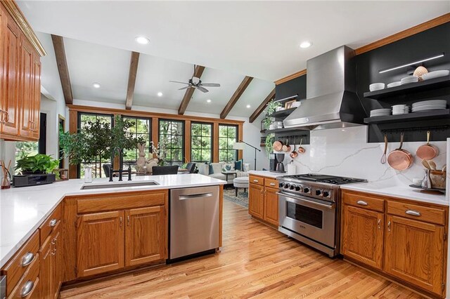 kitchen with wall chimney range hood, open shelves, appliances with stainless steel finishes, lofted ceiling with beams, and a sink