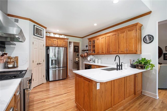 kitchen with a sink, a peninsula, light wood-style floors, stainless steel appliances, and wall chimney exhaust hood