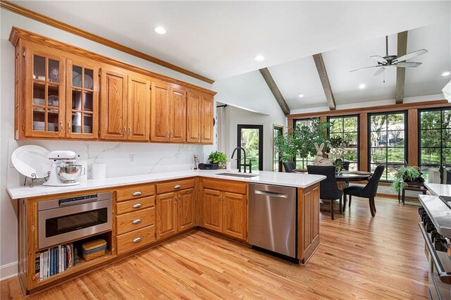 kitchen featuring brown cabinetry, a peninsula, vaulted ceiling with beams, a sink, and appliances with stainless steel finishes