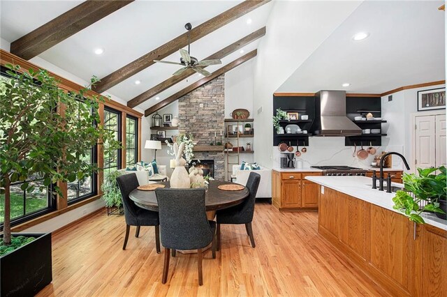 dining space with light wood-style floors, a stone fireplace, a ceiling fan, recessed lighting, and beamed ceiling