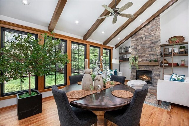 dining space with a ceiling fan, a stone fireplace, light wood-type flooring, and beam ceiling