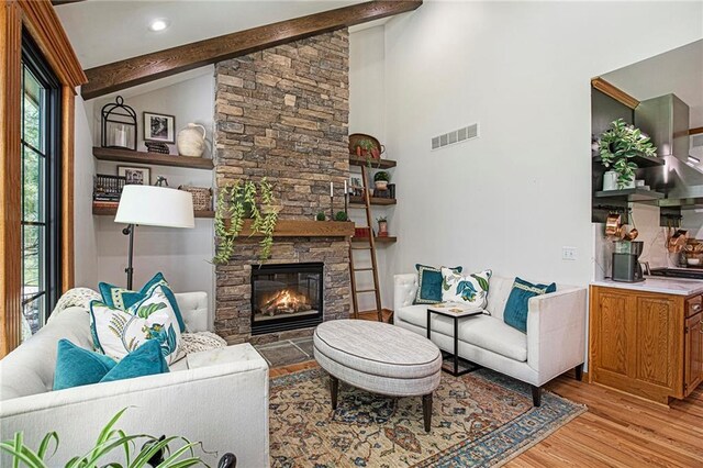 living area with light wood-type flooring, lofted ceiling with beams, visible vents, and a fireplace
