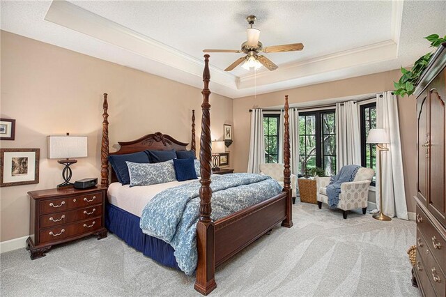 bedroom with ornamental molding, light carpet, and a tray ceiling