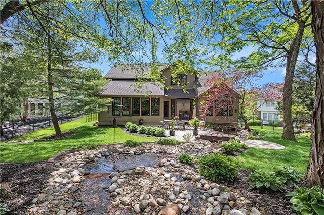 back of house featuring a shingled roof, a sunroom, a small pond, a patio area, and a yard