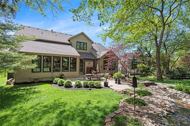 back of property with a lawn, a patio area, and roof with shingles