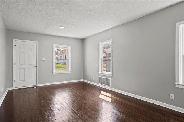 empty room with visible vents, hardwood / wood-style flooring, baseboards, and a textured ceiling