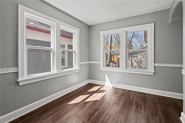 unfurnished room with baseboards, a textured ceiling, and dark wood finished floors