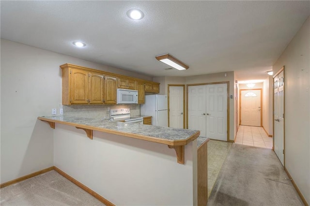 kitchen featuring light carpet, light countertops, a peninsula, a breakfast bar, and white appliances