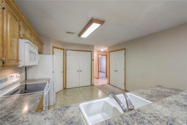 kitchen with a textured ceiling, visible vents, brown cabinets, a sink, and white appliances
