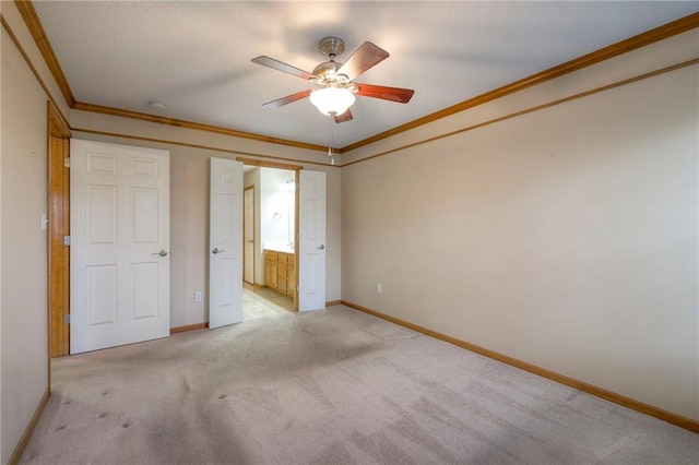 unfurnished bedroom with ceiling fan, baseboards, ornamental molding, ensuite bathroom, and light carpet
