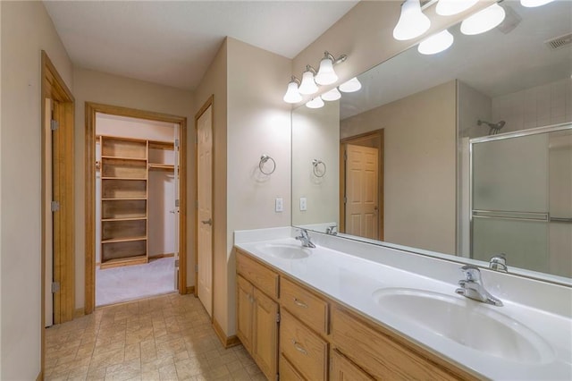 bathroom featuring double vanity, a shower with door, a spacious closet, and a sink