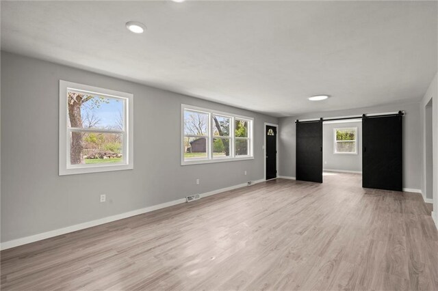 unfurnished living room featuring a barn door, visible vents, baseboards, and a healthy amount of sunlight