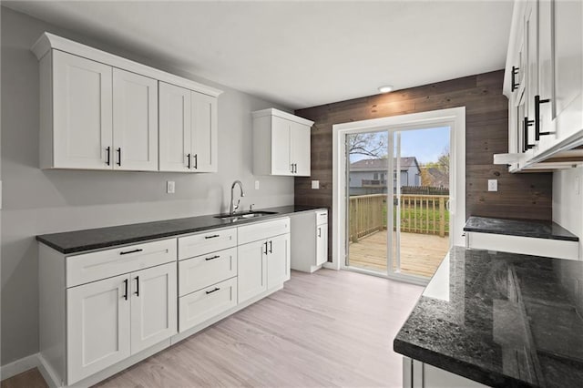 kitchen featuring light wood-type flooring, a sink, white cabinetry, and dark stone countertops