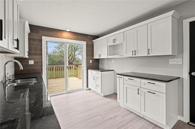 kitchen with dark stone countertops, a sink, white cabinetry, and light wood-type flooring