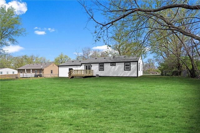 rear view of property featuring a wooden deck, fence, and a lawn