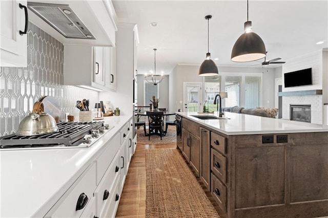 16955 W 168th Ter, Olathe, KS 66062 - kitchen featuring stainless steel gas cooktop, a sink, ceiling fan with notable chandelier, white cabinetry, and wall chimney range hood