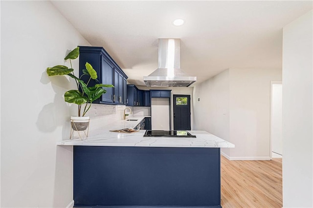 kitchen featuring island range hood, a peninsula, black electric cooktop, light wood finished floors, and light stone counters