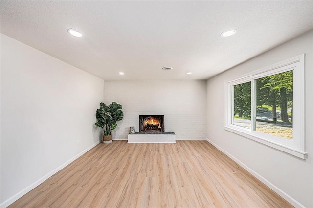 unfurnished living room with light wood-type flooring, a brick fireplace, baseboards, and recessed lighting