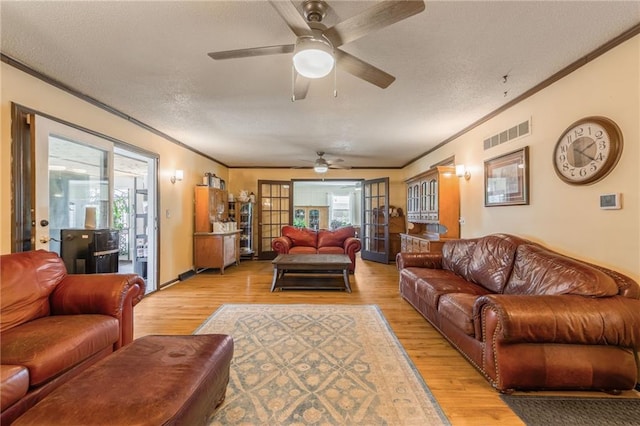 living area with ornamental molding, ceiling fan, light wood finished floors, and a textured ceiling