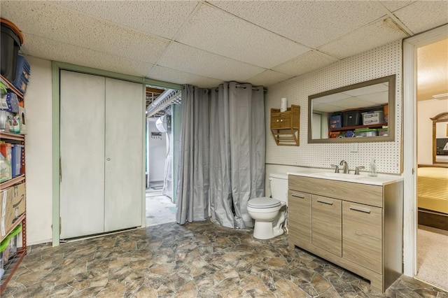 bathroom with toilet, stone finish floor, a drop ceiling, and vanity