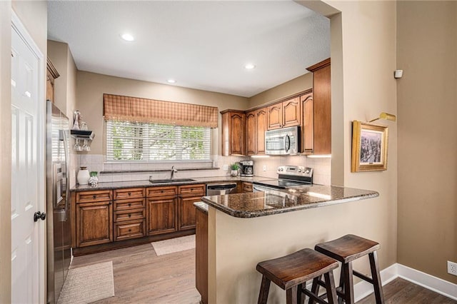 kitchen featuring a sink, brown cabinetry, stainless steel appliances, a peninsula, and a kitchen bar