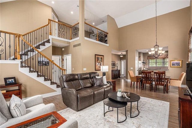 living area featuring a high ceiling, a chandelier, wood finished floors, visible vents, and stairway