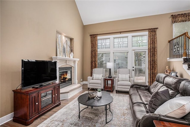 living room with baseboards, vaulted ceiling, a tile fireplace, and wood finished floors