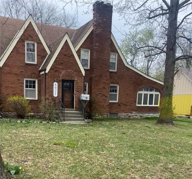 english style home featuring a chimney, brick siding, and a front lawn
