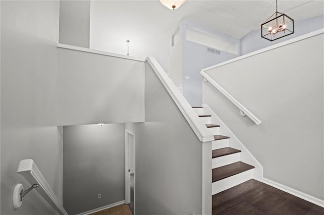 staircase featuring baseboards, wood finished floors, a notable chandelier, and visible vents