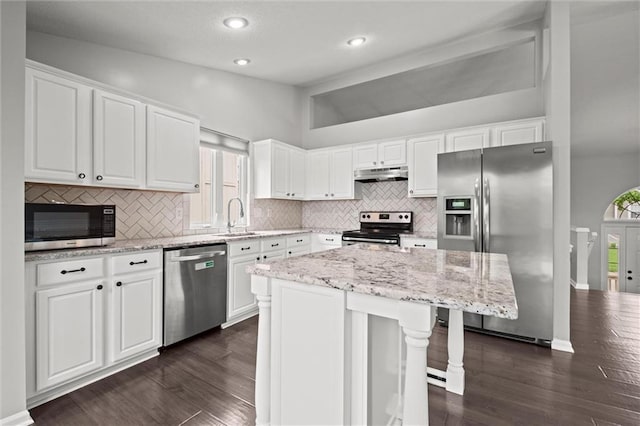 kitchen with dark wood-style flooring, under cabinet range hood, tasteful backsplash, and stainless steel appliances