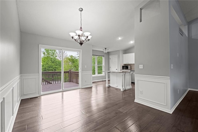 unfurnished dining area with a decorative wall, a chandelier, dark wood-type flooring, and a wainscoted wall