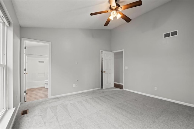 unfurnished bedroom featuring visible vents, baseboards, ensuite bathroom, carpet flooring, and vaulted ceiling