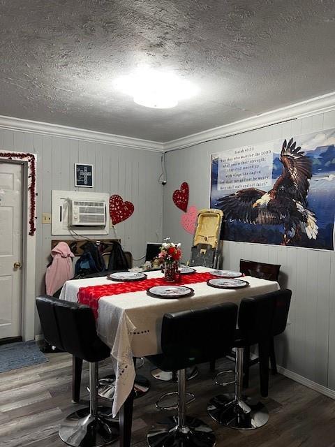 dining area featuring wood walls, wood finished floors, a textured ceiling, and ornamental molding