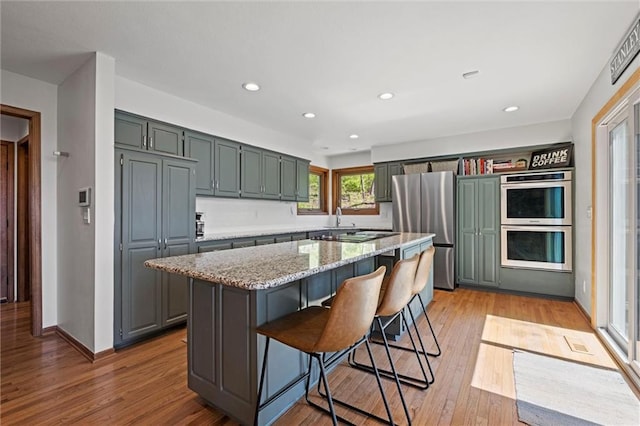 kitchen featuring appliances with stainless steel finishes, light stone counters, light wood-style floors, a breakfast bar area, and a kitchen island