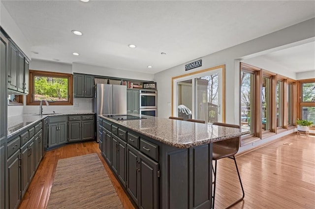 kitchen featuring a breakfast bar, light stone countertops, a center island, a sink, and light wood-style flooring
