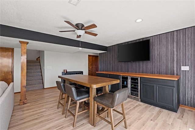 dining space featuring beverage cooler, baseboards, a dry bar, and light wood-type flooring