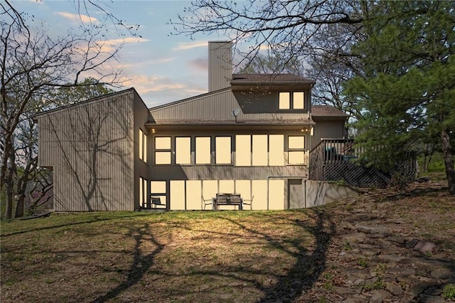 back of property at dusk with a chimney and a deck