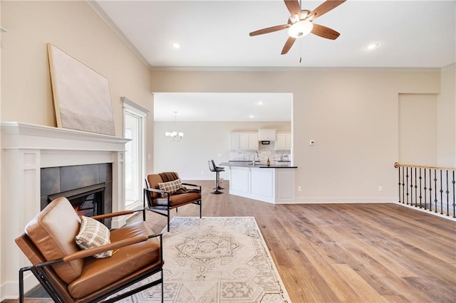 9331 N Belton Ave, Kansas City, MO 64154 - living room featuring a tile fireplace, baseboards, ceiling fan with notable chandelier, light wood-style floors, and ornamental molding