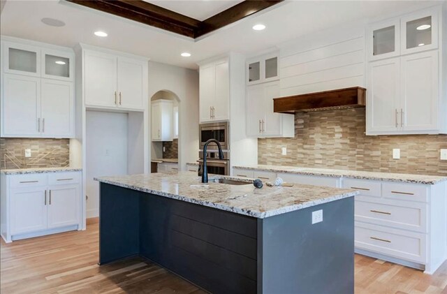 3217 SW Saddlebred Ter, Lees Summit, MO 64082 - kitchen featuring stainless steel appliances, light wood-type flooring, decorative backsplash, an island with sink, and white cabinets