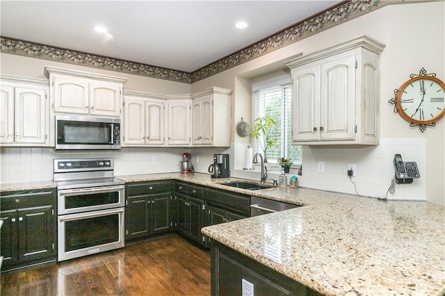 kitchen with a sink, appliances with stainless steel finishes, dark wood-type flooring, decorative backsplash, and light stone counters