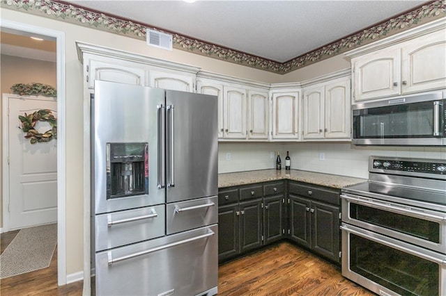 kitchen featuring light stone countertops, dark wood-type flooring, visible vents, stainless steel appliances, and backsplash