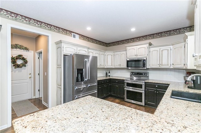 kitchen with visible vents, a sink, dark wood-style flooring, stainless steel appliances, and light stone counters