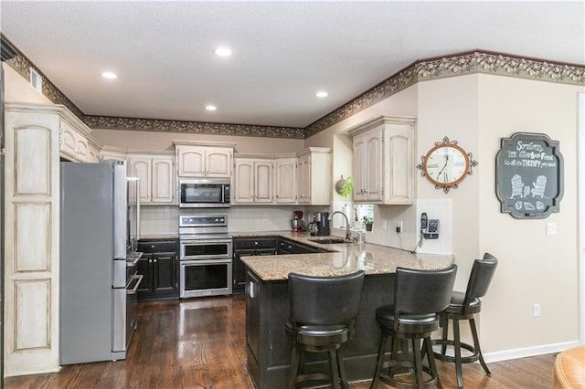 kitchen with dark wood-style flooring, a peninsula, a breakfast bar area, appliances with stainless steel finishes, and a sink