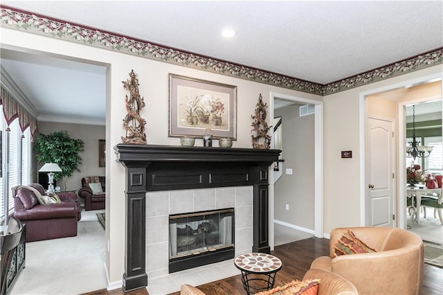 living room featuring baseboards, ornamental molding, visible vents, a tile fireplace, and wood finished floors