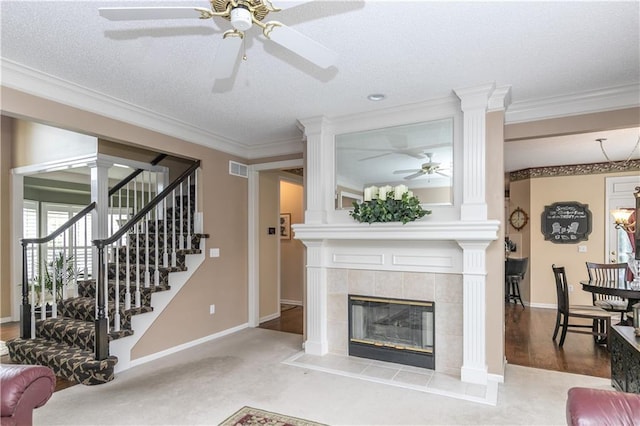 living room with baseboards, a tiled fireplace, stairway, a ceiling fan, and crown molding